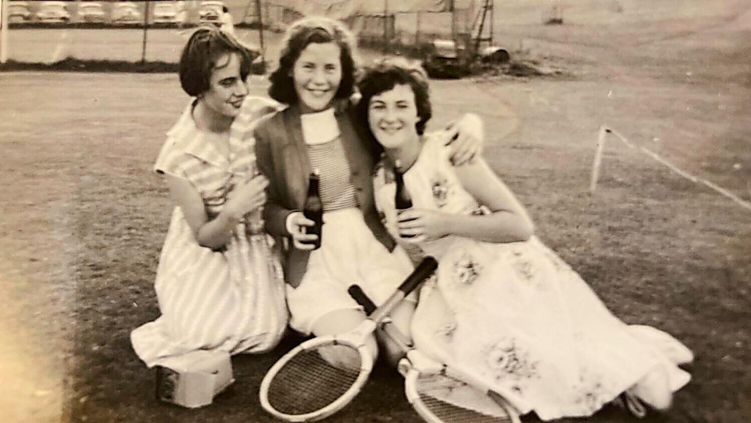 Three club members in dresses with wooden racquets on the grass court, 1950s
